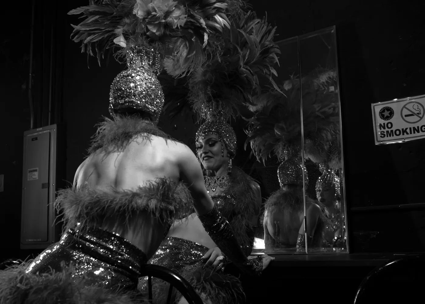 A performer in feathers and sequins at a backstage dressing mirror