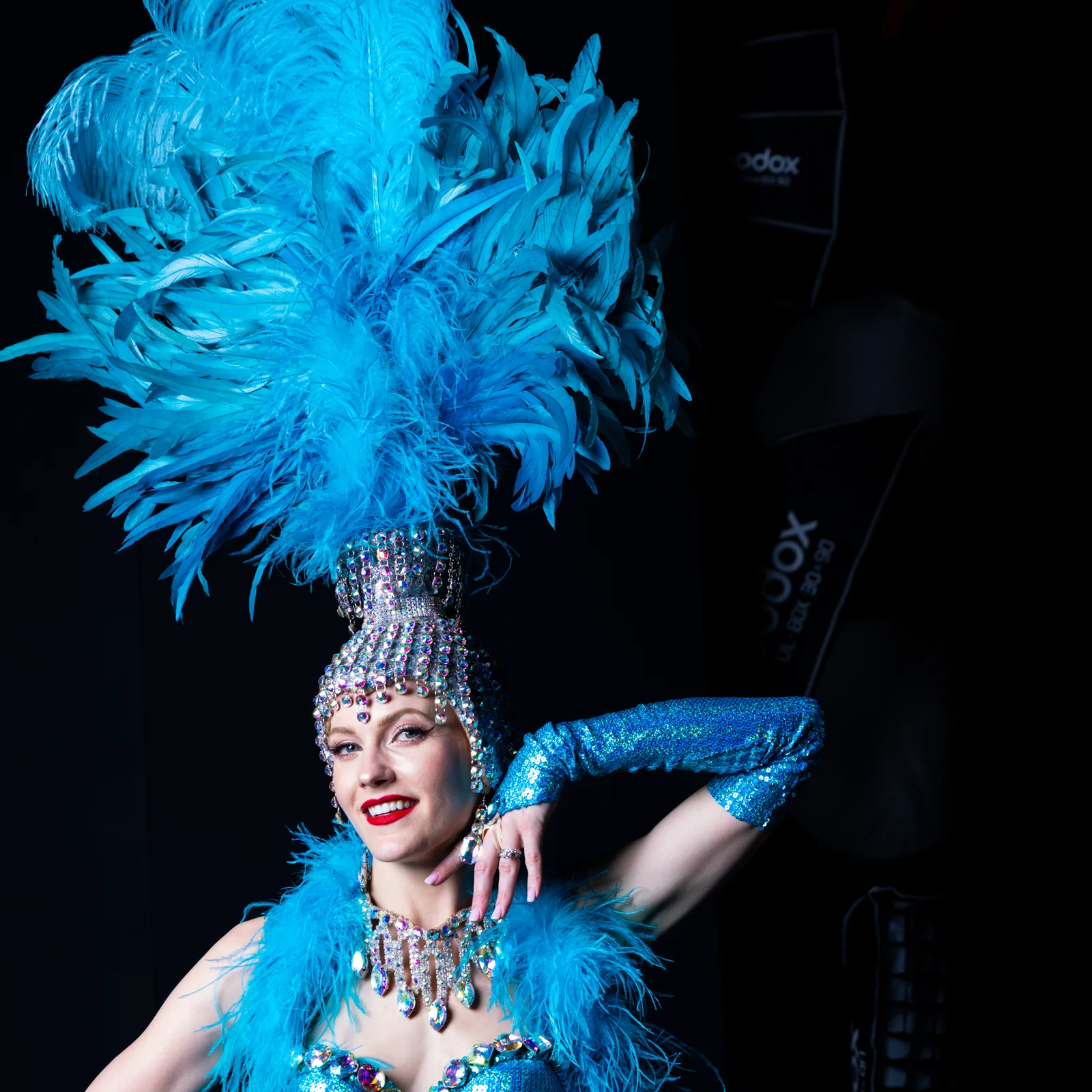 A showgirl in a feathered headdress and sequinned costume, lit against a dark stage